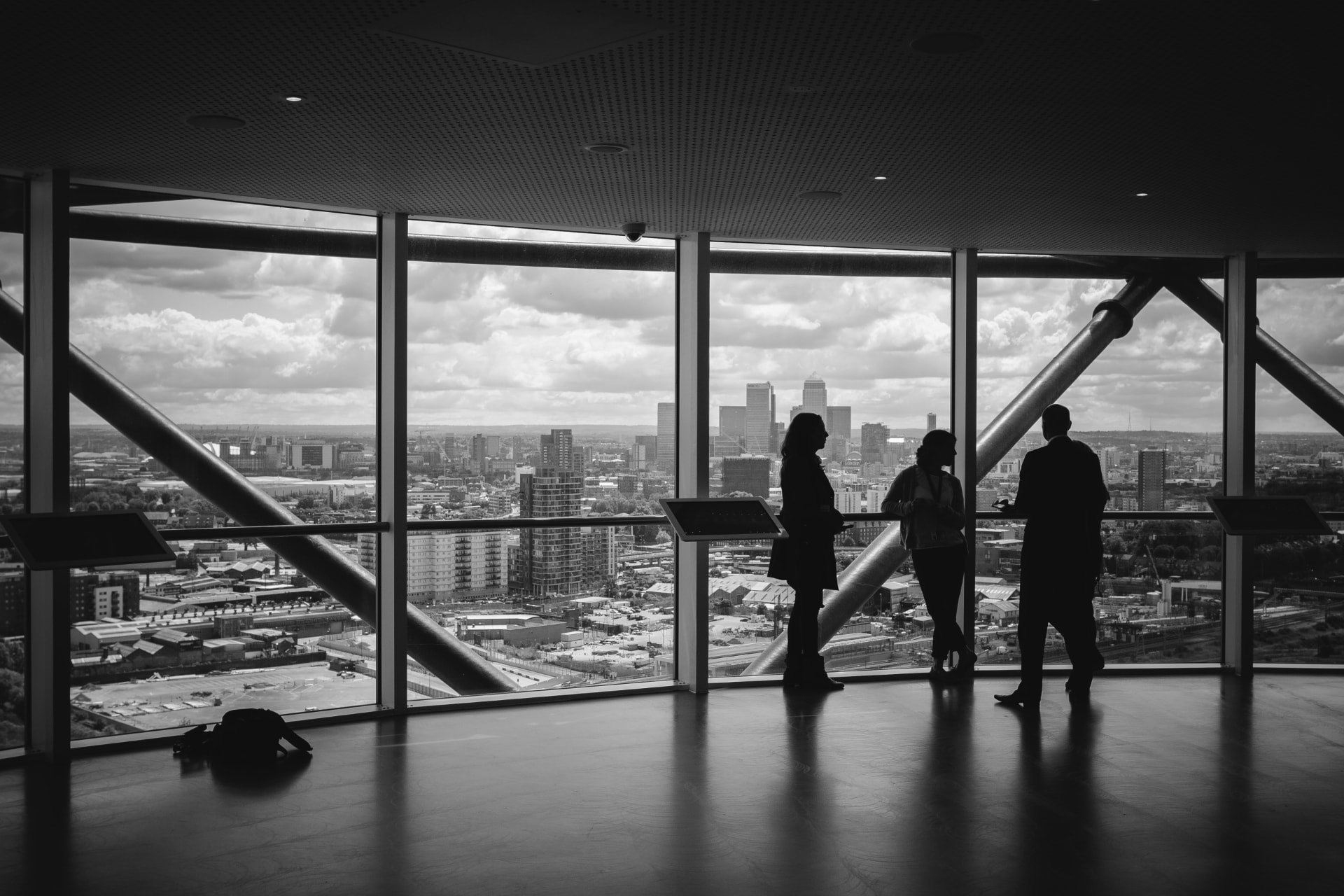 Three people in silhouette talking beside floor to ceiling windows overlooking a city skyline